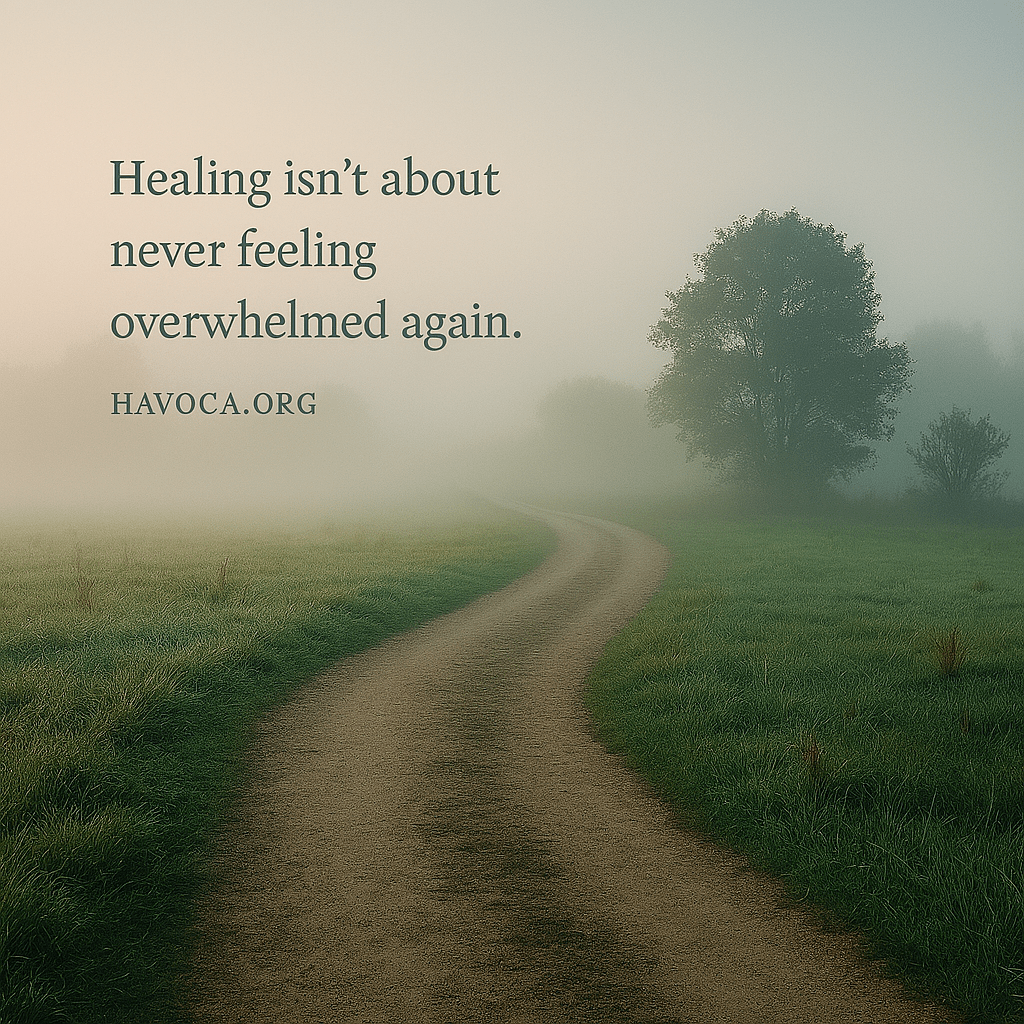 A misty woodland path curves gently through a quiet, fog-covered field at dawn. Soft light filters through the haze, illuminating dewy grass and a solitary tree on the right. Overlayed text reads: “Healing isn’t about never feeling overwhelmed again.” with “HAVOCA.ORG” beneath it. The scene evokes calm, reflection, and emotional depth.